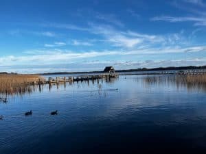 Steg am Hemmelsdorfer See unter blauem Himmel und spiegelglattem Wasser