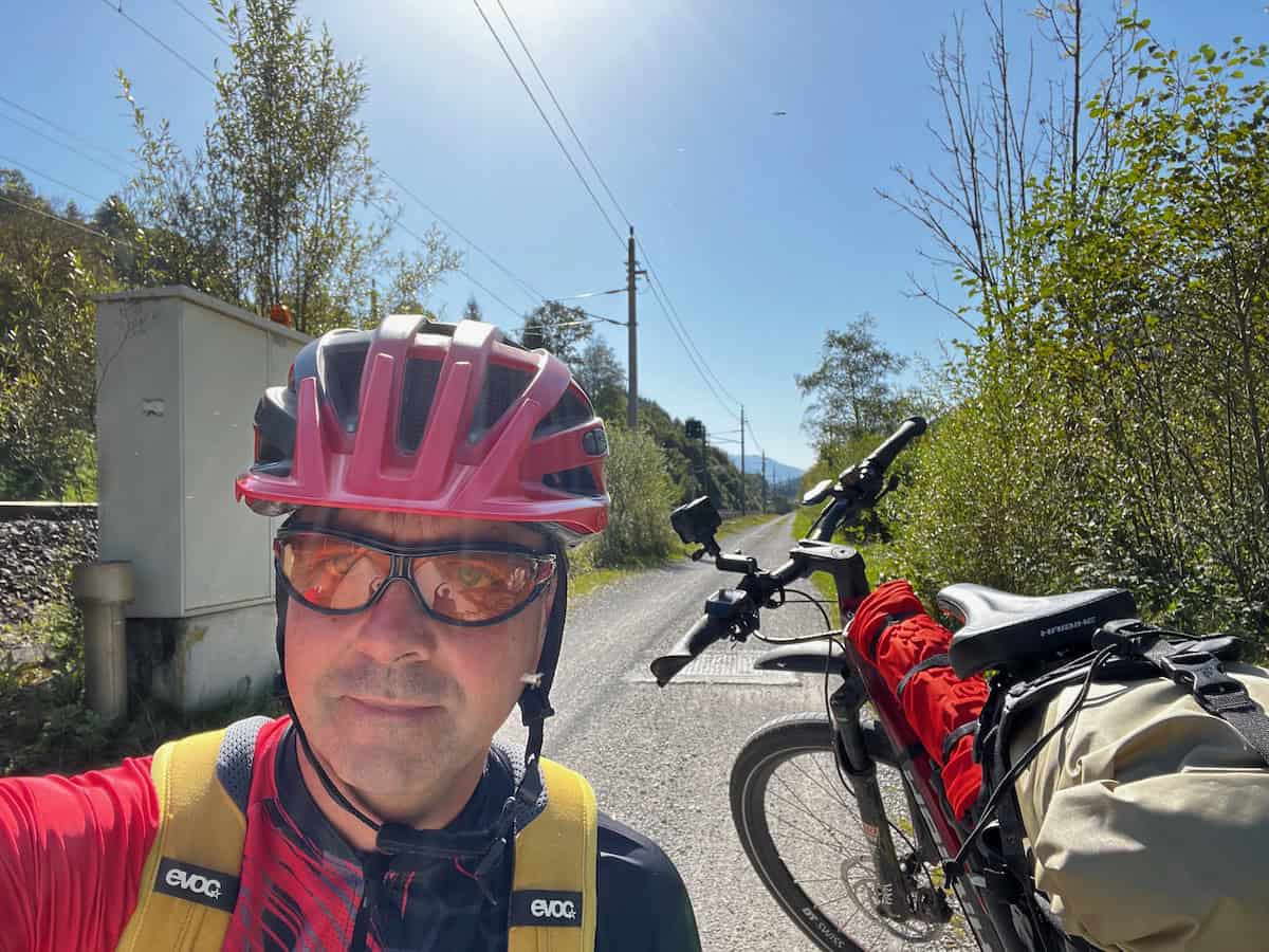 Selbstportrait eines Radreisenden mit voll bepacktem Fahrrad auf ruhiger Landstraße in den Bergen