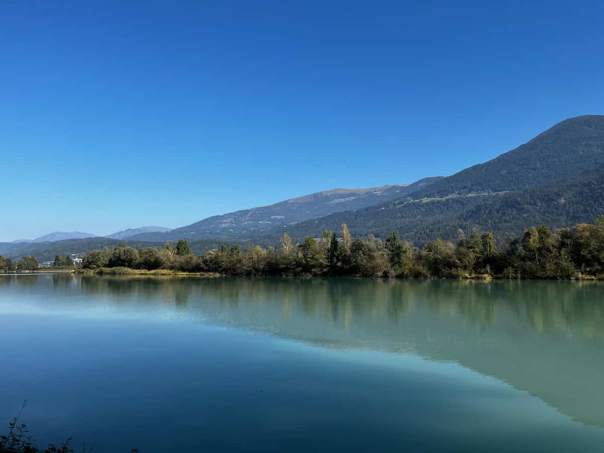 Spiegelglatte Wasserfläche der Drau vor alpiner Kulisse