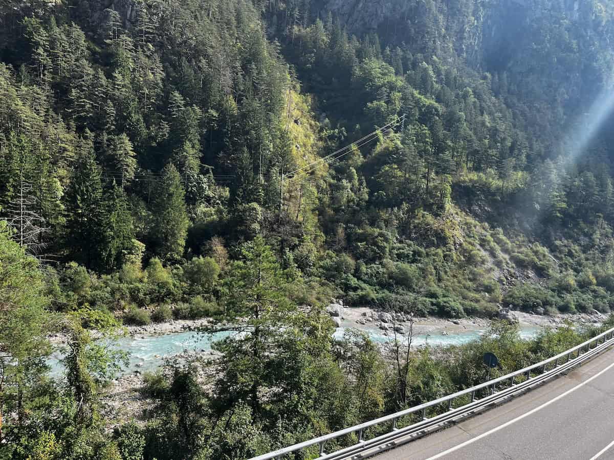 Gebirgsfluss mit Straße im Vordergrund, typische Landschaft entlang der Alpenetappen