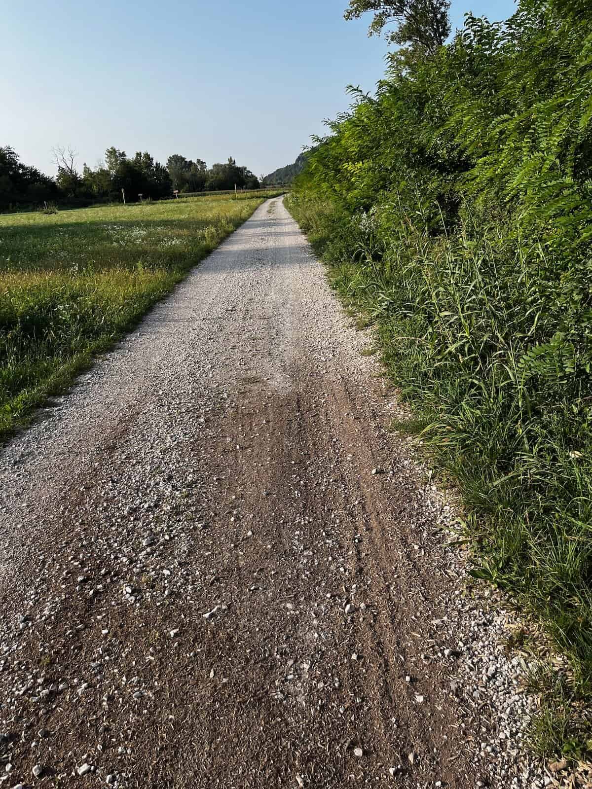Schotterweg durch grüne Landschaft in Italien, Radfahren auf dem Alpe Adria Radweg Richtung Udine